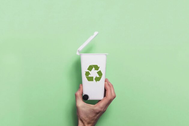 Hand holding recycling rubbish bin against a green background